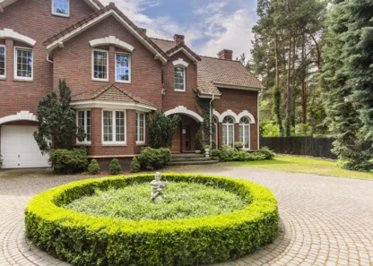 Brick house with round hedge and statue in front yard
